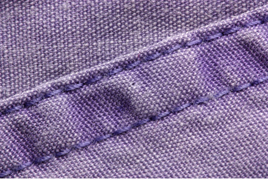 Close-up of a flat-felled seam showing clean, professional stitching on lavender fabric.