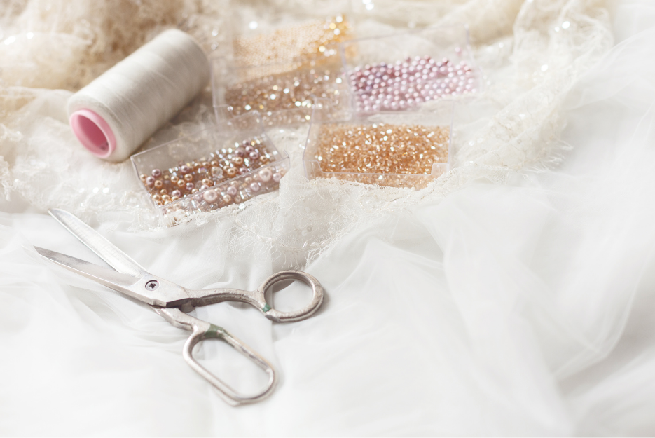 Lace fabric, beads, and sewing shears arranged on a white surface, representing delicate sewing materials