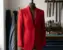 A vibrant red 80s-inspired structured jacket on a vintage wooden dress form in a sewing studio, showcasing a balanced T-frame silhouette.