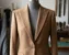 A camel-colored tailored wool blazer on a dress form, showcasing a crisp "T-frame" silhouette that balances the shoulders and hips.