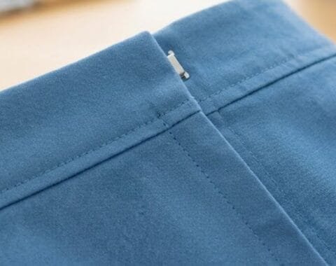 Close-up of a lapped zipper installed in blue fabric, showing the folded overlap and hidden stitching line
