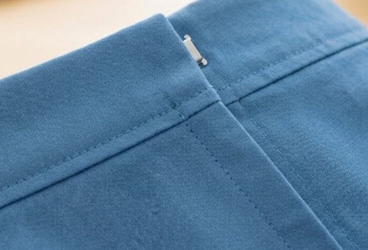 Close-up of a lapped zipper installed in blue fabric, showing the folded overlap and hidden stitching line