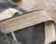 Close-up of a tailored trouser waistband under construction, showing the cream interfacing and facing folded back to reveal the interior stitching against gray wool fabric.