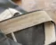 Close-up of a tailored trouser waistband under construction, showing the cream interfacing and facing folded back to reveal the interior stitching against gray wool fabric.